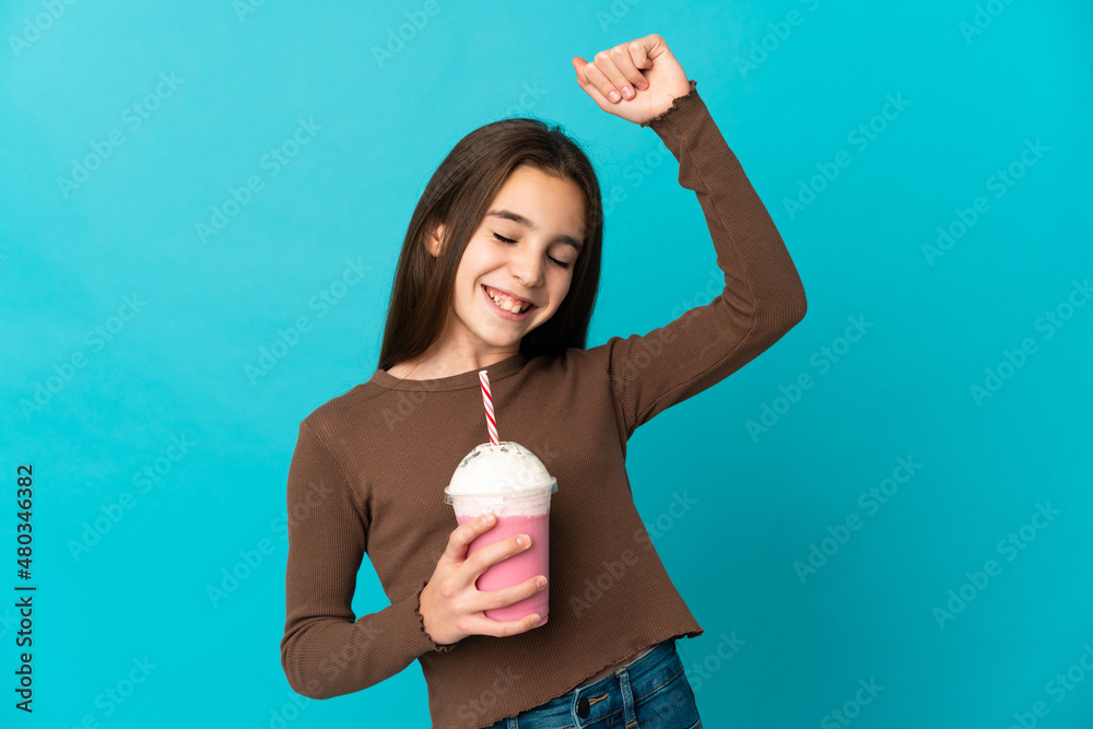 Little girl with strawberry milkshake isolated on blue background celebrating a victory Little girl with strawberry milkshake isolated on blue background celebrating a victory