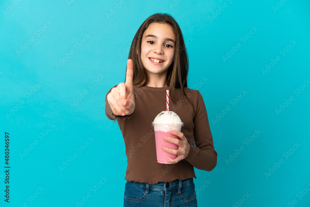 Little girl with strawberry milkshake isolated on blue background showing and lifting a finger Little girl with strawberry milkshake isolated on blue background showing and lifting a finger