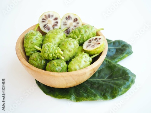 Fresh noni fruit or morinda citrifolia and slices in wood bowl on white background. closeup photo, blurred.