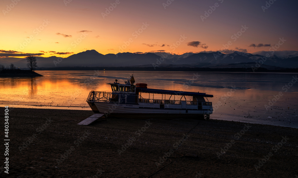 Ship on the shore of lake and beautiful colorful sky in the cold morning. Sunrise in bright colors on Dam Liptovska Mara, Slovakia Ship on the shore of lake and beautiful colorful sky in the cold morning. Sunrise in bright colors on Dam Liptovska Mara, Slovakia