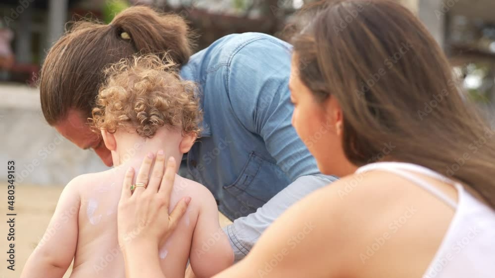 Caucasian family parents with little child boy enjoy outdoor lifestyle on summer holiday travel vacation. Father and mother applying sunblock to cute baby son before playing together on tropical beach Caucasian family parents with little child boy enjoy outdoor lifestyle on summer holiday travel vacation. Father and mother applying sunblock to cute baby son before playing together on tropical beach