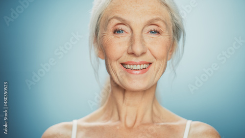 Close-up Portrait of Beautiful Senior Woman Looking at Camera and Smiling Wonderfully. Gorgeous Elderly Lady with Natural Lush Grey Hair  Blue Eyes. Beauty and Dignity of Old Age