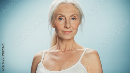Portrait of Beautiful Senior Woman Looking at Camera and Smiling Wonderfully. Elderly Lady with Natural Lush Grey Hair, Blue Eyes, Wearing Top. Beauty and Dignity of Old Age