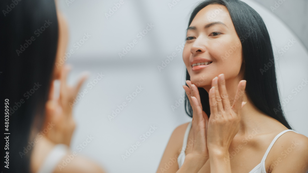 Portrait of Beautiful Asian Woman Gently Applying Face Cream Looking in Bathroom Mirror. Young Adult Female Makes Her Skin Soft, Smooth, Wrinkle Free with Natural Cosmetics Skincare Product Portrait of Beautiful Asian Woman Gently Applying Face Cream Looking in Bathroom Mirror. Young Adult Female Makes Her Skin Soft, Smooth, Wrinkle Free with Natural Cosmetics Skincare Product