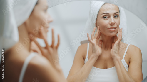 Beautiful Caucasian Woman Touches Her Perfect Soft Shoulder, Neck, Sensually Looks in Bathroom Mirror. Middle Aged Female Enjoying Her Natural Beauty Morning Routine. Over Shoulder Shot