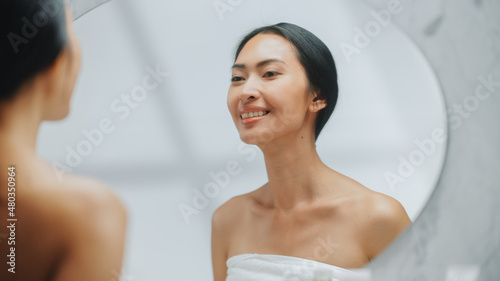 Portrait of Beautiful Asian Woman Checking her Clean Naturaly White Teeth, Smiles in Bathroom Mirror. Happy Female Enjoying Morning routine. Dental Hygiene, Wellness, beauty. photo