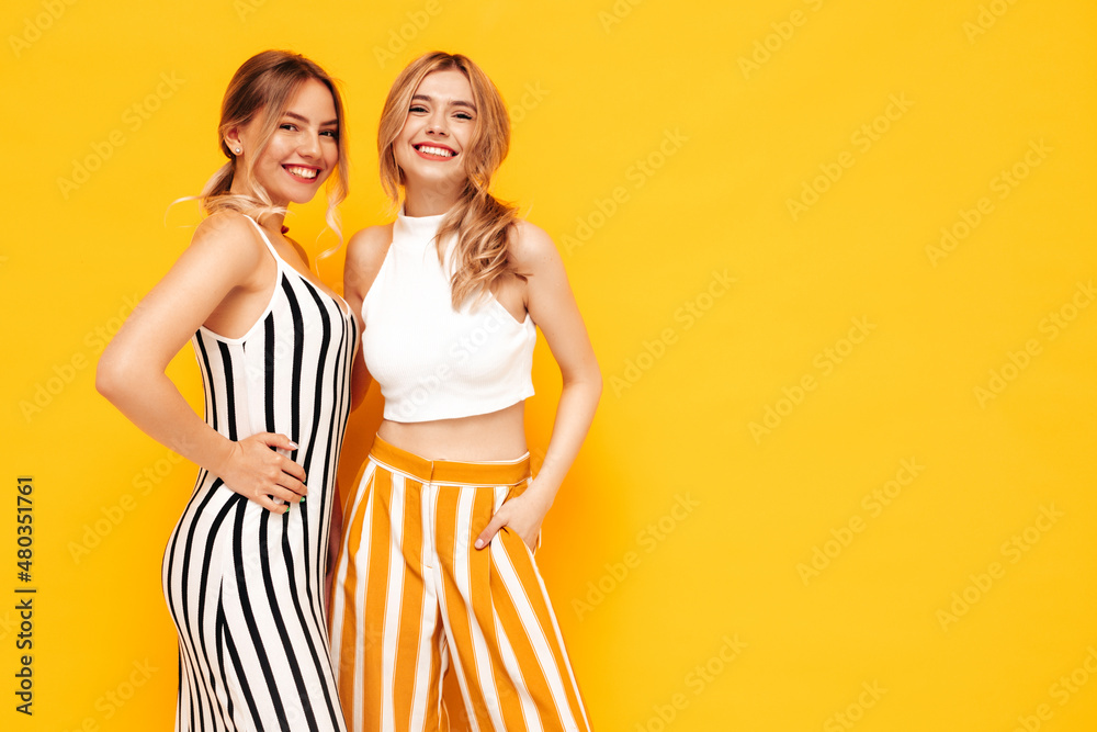 Two young beautiful smiling brunette hipster female in trendy summer clothes. Sexy carefree women posing near yellow wall in studio. Positive models having fun. Cheerful and happy Two young beautiful smiling brunette hipster female in trendy summer clothes. Sexy carefree women posing near yellow wall in studio. Positive models having fun. Cheerful and happy