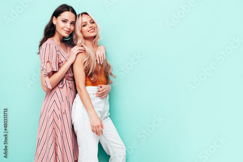 Two young beautiful smiling brunette hipster female in trendy summer dresses. Sexy carefree women posing near blue wall. Positive models having fun. Cheerful and happy