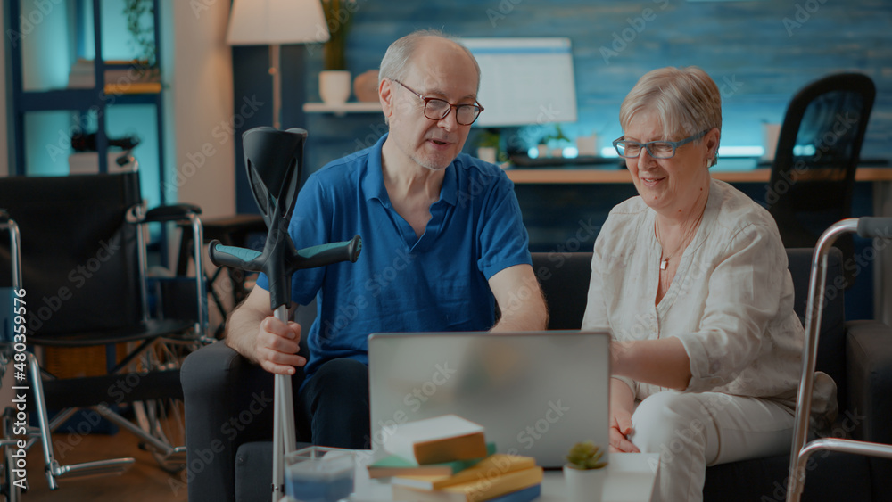 Senior people giving high five and celebrating successful teamwork on laptop at home. Retired man and woman with disability feeling positive about success on computer. Walking support