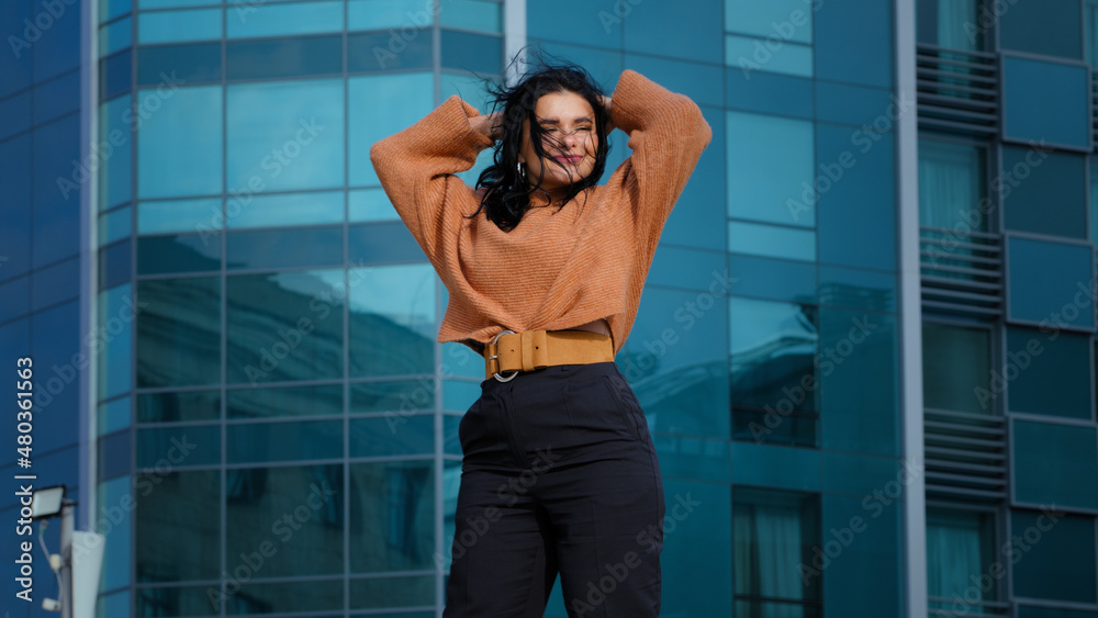 Happy carefree young woman brunette model actively dancing outdoors on city building background funny joyful hispanic girl student smiling rhythmically moving winner dance enjoying weekend freedom