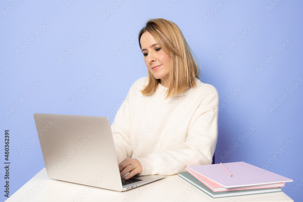 Young cheerful woman using laptop and sit at the table on her workplace isolated over purple background. Young cheerful woman using laptop and sit at the table on her workplace isolated over purple background.