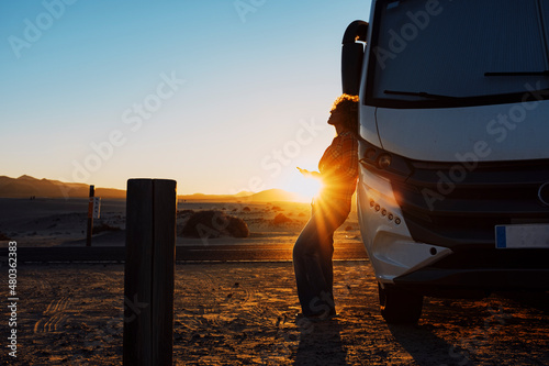 Happiness and freedom life with woman against camper van and golden sunset in background. People enjoying vanlife and summer holiday vacation with big camping car parked off road. Alone traveler