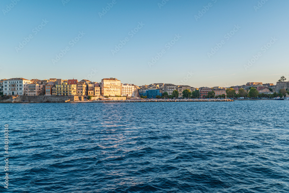 Buildings of Corfu island on shore and sea water at sunset
