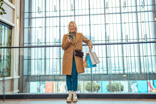 Young woman using mobile phone while holding shopping bag in department store. Consumerism and lifestyle concept. Sale  consumerism  technology and people concept