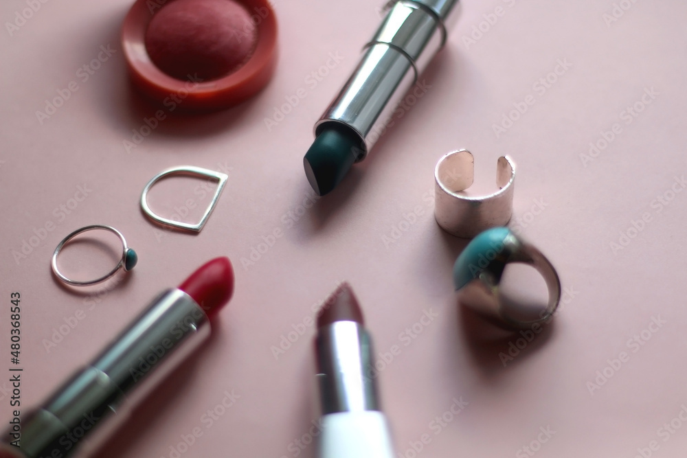Various lipsticks, pink blush and silver rings on bright pink background. Selective focus. Various lipsticks, pink blush and silver rings on bright pink background. Selective focus.