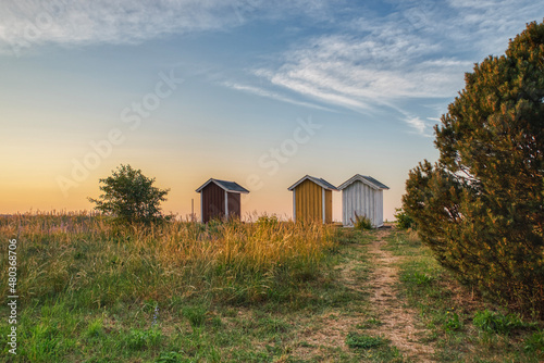Three small rustic summerhouses at sunset on a strand show nordic summer vacation or Scandinavian holiday illustration. 3 wooden summer houses at dusk on a Swedish beach convey a comfort zone concept