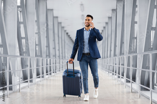 Φωτογραφία Handsome Arab Man Walking With Suitcase In Airport And Talking On Cellphone