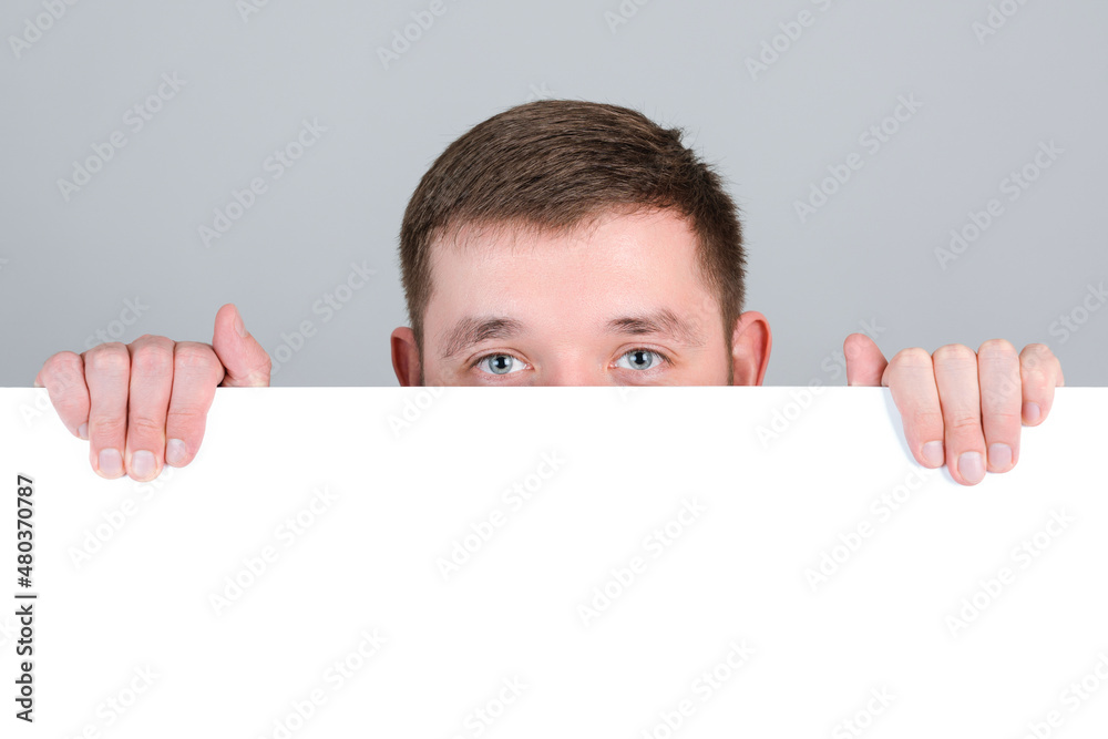 A red-haired man looks out from behind a white blank board A red-haired man looks out from behind a white blank board