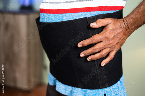 close up shot of unrecognizable senior man using back pain relief belt or brace at home - concept of relax from using back supoort belt, spine treatment and healing injury photo