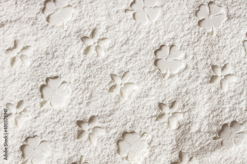 Texture of white fine flour powder with small flower print. Handmade flower pattern. Silhouette of the blooming flower on layer of flour Abstract background. Top view on white background.