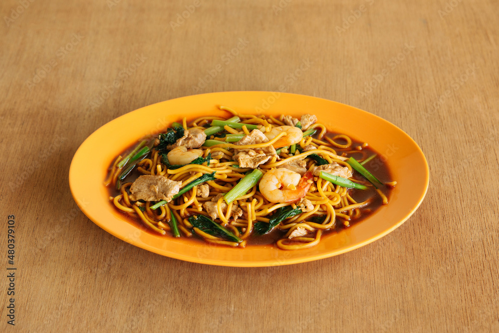Delicious Singapore style Hokkien Mee noodles shrimps in orange plate on wooden background top view