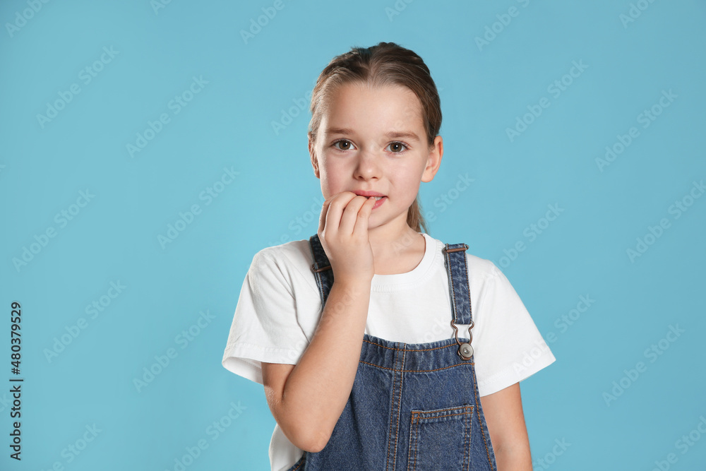 Cute little girl biting her nails on turquoise background Cute little girl biting her nails on turquoise background