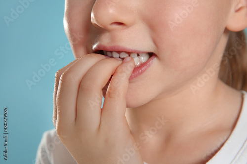 Little girl biting her nails on turquoise background  closeup
