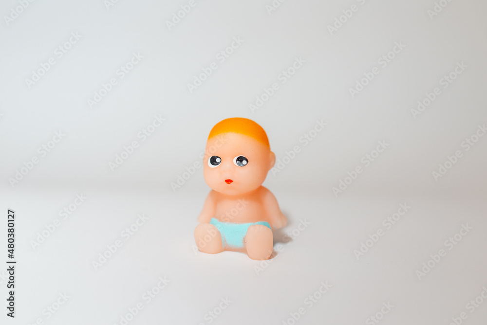 Miniature newborn infant baby toy sitting on a white gray background.Selective focus,copy space. Miniature newborn infant baby toy sitting on a white gray background.Selective focus,copy space.