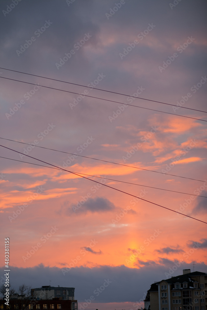 Bright colorful sunset through the wires over the city with dark silhouettes of the buildings. Vertical sky backgroud at sunset or sunrise