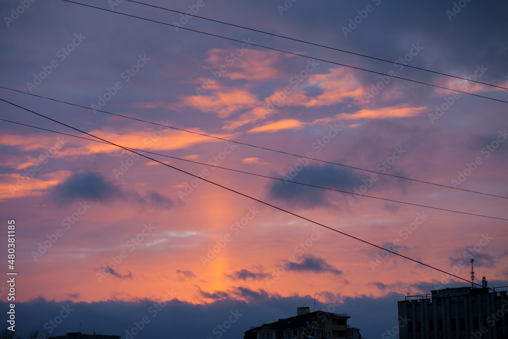 Bright colorful sunset through the wires over the city with dark silhouettes of the buildings. Horizontal sky backgroud at sunset or sunrise