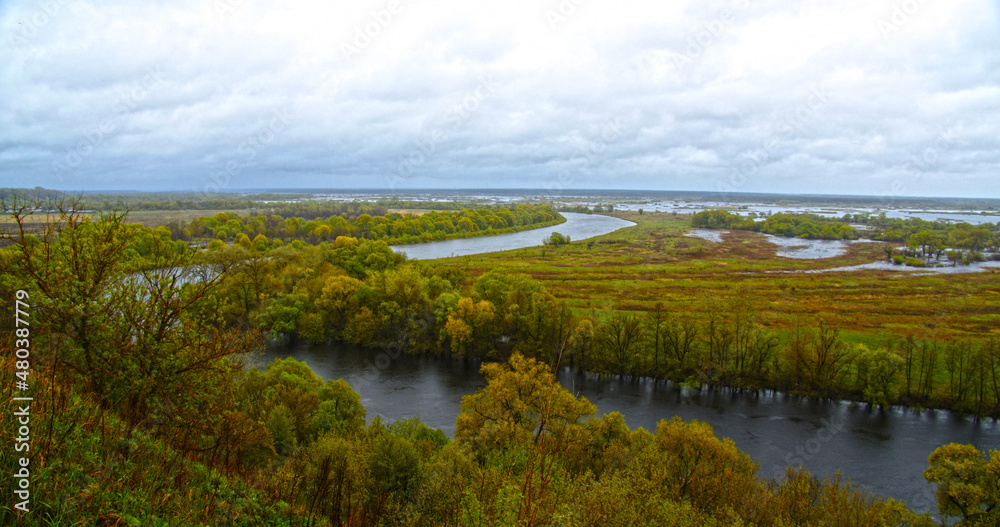 Beautiful summer landscape on a cloudy day. View from the hill to the winding river in rainy weather. View from  height of the meadow flooded after the flood in spring. Nature and landscape in Europe
