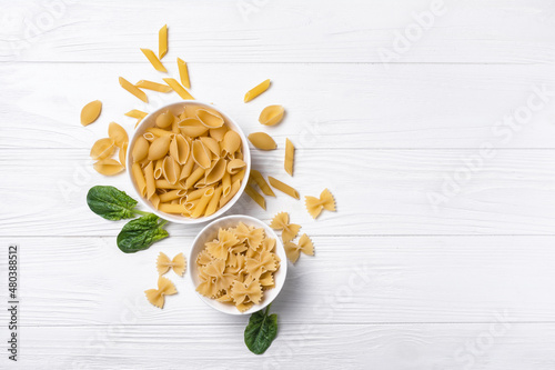 Mix of Italian raw pasta in white bowls with spinach leaves