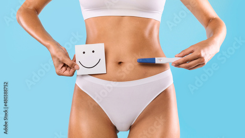 Woman holding pregnancy test and card with smiley face
