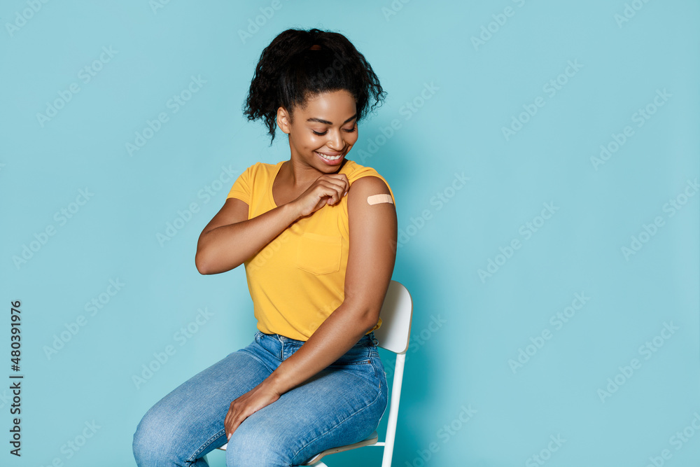 Smiling black woman getting vaccinated against covid, showing arm with band aid on blue background, free space - obrazy, fototapety, plakaty 