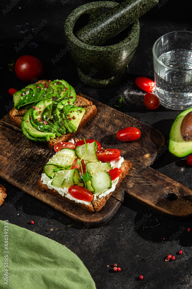 Toast with cream cheese, avocado, cucumber and tomato on a table