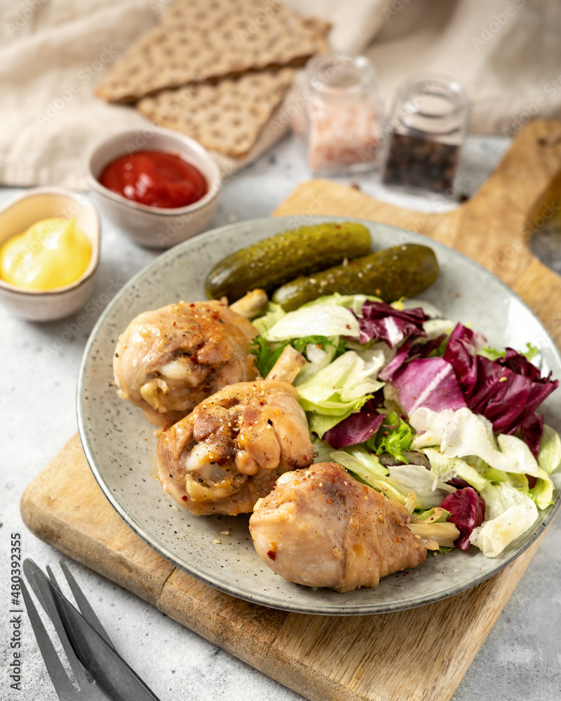 Fried chicken legs with salad and pickles in a plate on a light gray kitchen table. Cooked poultry meat in close-up on a culinary background Fried chicken legs with salad and pickles in a plate on a light gray kitchen table. Cooked poultry meat in close-up on a culinary background
