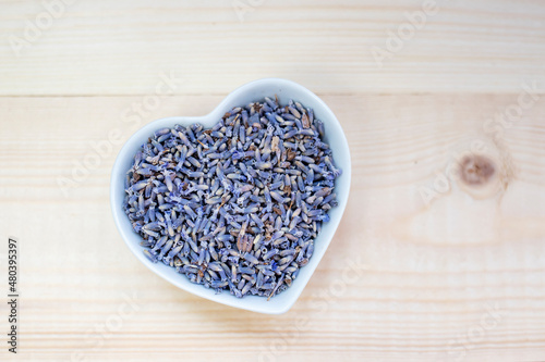 Dried lavender flowers in a bowl on a wooden background. Flat lay, place for text.