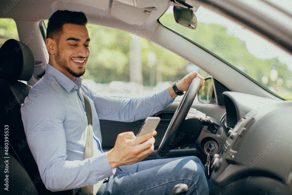 Cheerful arab man using cellphone while driving car Cheerful arab man using cellphone while driving car
