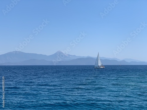 Yacht with a white sail in the open sea. A sailboat sails in the ocean off the coast. Boat with a sail on the waves of a calm sea.