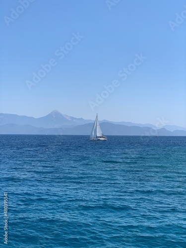 Yacht with a white sail in the open sea. A sailboat sails in the ocean off the coast. Boat with a sail on the waves of a calm sea.