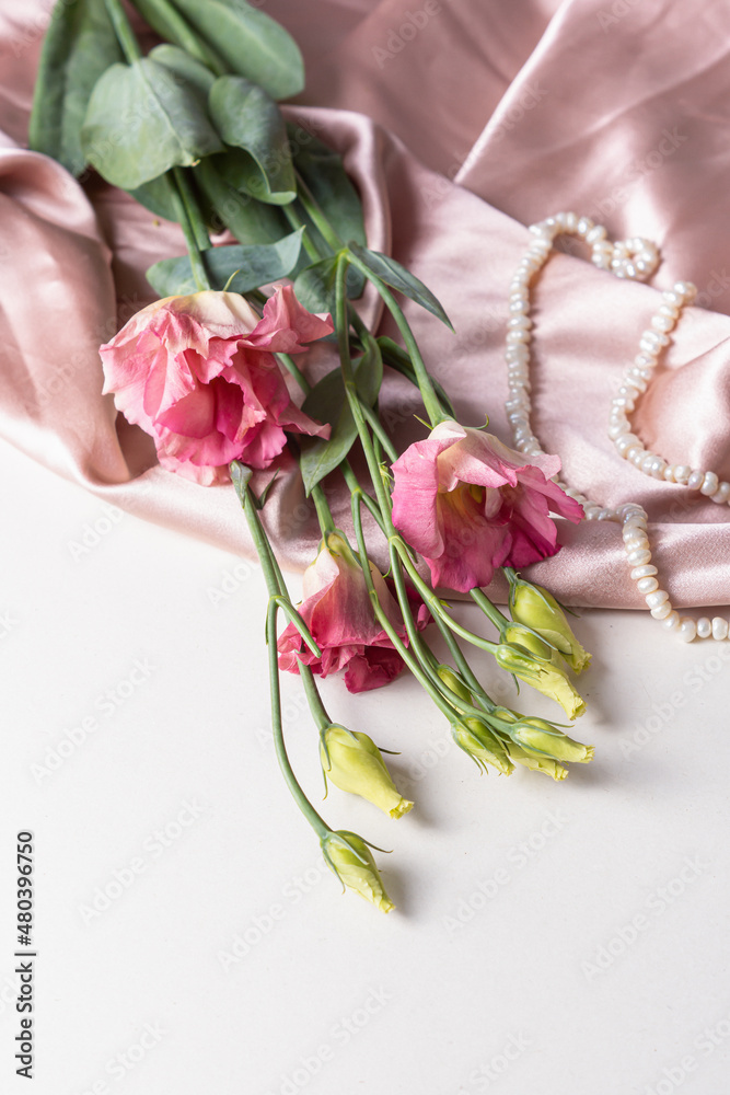Pink eustoma and pearl necklace. Twig of eustoma on silk background