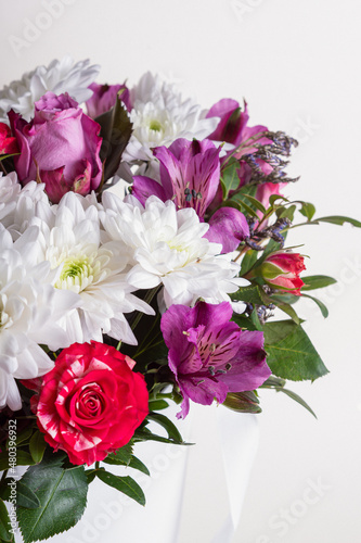 Floral arrangement in hat box on light background. Bouquet with red roses  white chrysanthemums and lilac alstroemeria