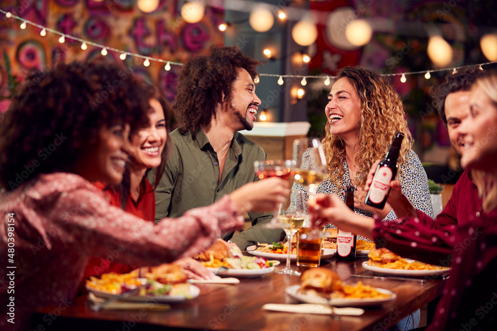 Multi-Cultural Group Of Friends Enjoying Night Out Eating Meal And Drinking In Restaurant Together