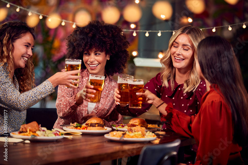 Multi-Cultural Group Of Female Friends Enjoying Night Out Eating Meal And Drinking In Restaurant