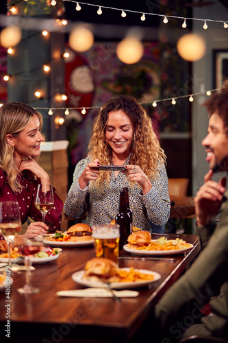 Multi-Cultural Group Of Friends Enjoying Night Out Taking Picture Of Food On Mobile Phone