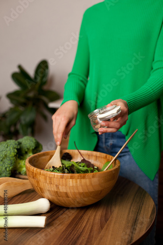 Woman in green shirt cooking a salad at home in the kitchen. making vegan dinner or lunch with fresh vegetables. Healthy and eco conscious vegetarian lifestyle.