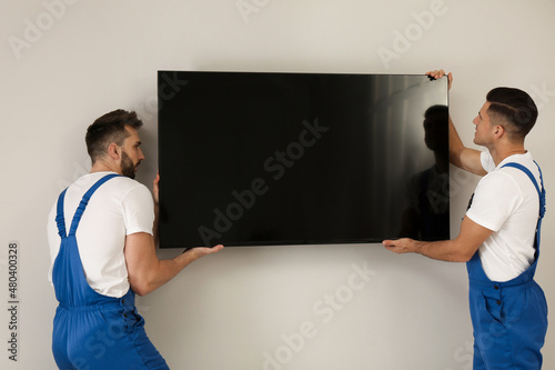 Professional technicians installing modern flat screen TV on wall indoors