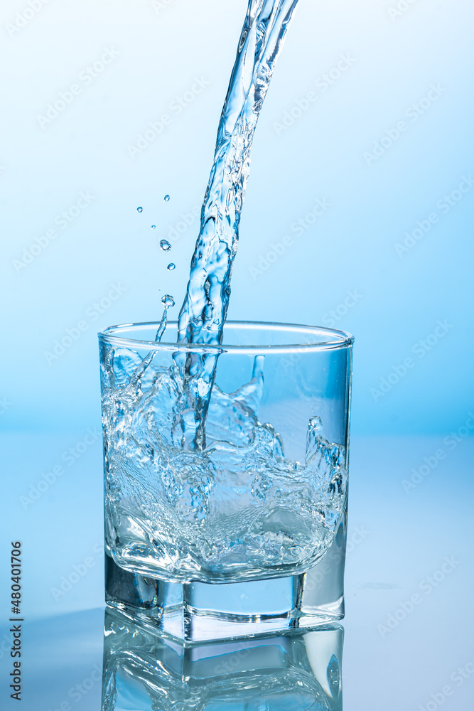 splash of water in a transparent glass on a blue background splash of water in a transparent glass on a blue background