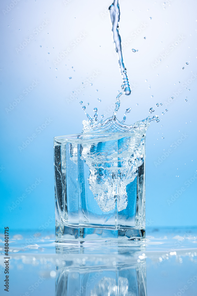 splash of water in a transparent glass on a blue background splash of water in a transparent glass on a blue background