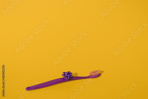 Single new isolated purple toothbrush with a ribbon bow on a bright vibrant yellow background with copy space. Minimal dental theme. Orthodontist medical mockup. Fun hygiene for kids. Very peri.
